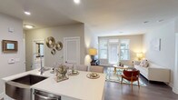 This single-story residence is designed with an open-concept floor plan that seamlessly connects the kitchen, dining, and living areas into one cohesive, light-filled space. Large windows fitted with white blinds allow generous natural light to fill the main living area, creating a bright and welcoming atmosphere throughout.

The kitchen is outfitted with crisp white shaker-style cabinetry extending to the ceiling, a classic white subway tile backsplash, stainless steel appliances including a range, built-in microwave, and French door refrigerator, and a light quartz countertop island with an undermount sink. Wood-look flooring runs throughout the main living areas, lending warmth and continuity.

A dedicated dining nook adjacent to the living space provides an intimate setting. The living room opens toward the front windows, enhancing the sense of openness.

Both bedrooms feature plush carpet flooring, ceiling fans, and windows with ample natural light. The primary bedroom connects to a full bathroom with a white vanity, tile flooring, and a tub-shower combination, alongside a walk-in closet with built-in shelving. An in-unit laundry closet with a washer adds everyday convenience to this thoughtfully designed residence.