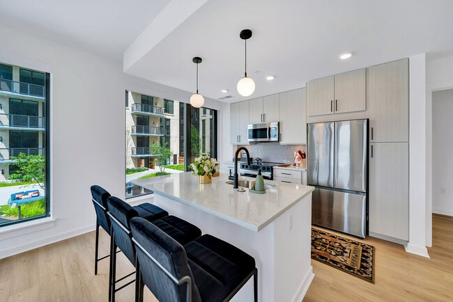 Kitchen with white island, stainless appliances, black barstools, pendant lights, and large windows and stainless steel appliances - Vermeer