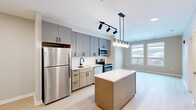 Located at 630 Kenilworth Terrace NE in Washington, DC, this thoughtfully designed one-bedroom, two-bathroom residence offers a modern and functional layout across a single floor. Light wood-tone flooring runs throughout, creating a cohesive and airy feel.

The open-concept kitchen is a standout feature, appointed with two-tone cabinetry — cool grey upper cabinets paired with warm wood lower cabinets — complemented by a white subway tile backsplash and stainless steel appliances, including a full-size refrigerator, range, microwave, and dishwasher. A central island with a clean white countertop provides additional prep space and casual dining. Track lighting and a pendant light fixture above the island add a contemporary touch, while large windows flood the adjoining living area with natural light and offer views of the surrounding neighborhood.

The bedroom is a calm, neutral-toned retreat featuring a window with outdoor views, light walls, and ample closet storage with louvered bi-fold doors. A connecting hallway leads efficiently between rooms.

The bathroom is finished with large-format tile flooring, a tub-shower combination with elegant matte black fixtures, and a wood-toned vanity with a white countertop, reflecting the modern design language carried throughout the home.