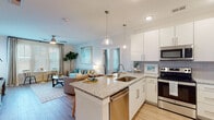 Located at 1749 Sea Pine Blvd in Myrtle Beach, SC, this single-floor residence offers a thoughtfully designed layout with a bright, coastal aesthetic. The open-concept kitchen and living area serves as the heart of the home, where a granite-topped island with an undermount sink and pendant lighting anchors the space. White shaker cabinetry, subway tile backsplash, and a full suite of stainless steel appliances — including a refrigerator, range, and over-the-range microwave — provide a clean, modern look. Light wood-style flooring flows throughout the main living areas, enhancing the airy feel. The living room benefits from generous natural light through large windows dressed with blinds and drapes, and features direct access to an outdoor area via a glass-paneled door. Multiple bedrooms are finished with plush carpet, ceiling fans, and large windows that fill each room with natural light. The primary bedroom connects to a private en-suite bath featuring a walk-in shower, granite vanity, and wood-look flooring. An additional full bathroom includes a tub-shower combination and matching granite countertops. Neutral warm tones and consistent finishes throughout lend the home a cohesive, inviting atmosphere well-suited to the coastal Myrtle Beach setting.