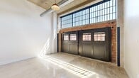 Located at 8 S Erie Street in Toledo's downtown district, this first-floor unit blends industrial character with modern finishes throughout its thoughtfully designed single-level layout. The most striking feature is the expansive main living area, where soaring ceilings, exposed concrete overhead, and visible silver ductwork establish a raw, industrial aesthetic. Oversized factory-style steel-framed windows run along the upper wall, flooding the space with natural light that reflects brilliantly off the polished concrete floors. A set of bold black carriage-style doors with windowed panels serves as a dramatic architectural focal point, framing street views while reinforcing the building's historic character. Exposed brick accents and original concrete columns further enhance the industrial ambiance.

The open kitchen features dark cabinetry, stainless steel appliances including a refrigerator, microwave, and range, and a central island with seating, all anchored by the same polished concrete flooring. Private rooms transition to soft carpeting underfoot, offering a quieter, more intimate atmosphere, with an exposed concrete column adding a rustic touch. The full bathroom is cleanly appointed with a dark-vanity cabinet, white countertop, industrial-style wall sconces, and a tub-shower combination, complemented by polished concrete flooring.