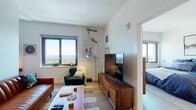 Located in New Rochelle, NY, this one-bedroom, one-bathroom residence at 360 Huguenot St offers a well-designed contemporary living space with striking elevated views of the surrounding cityscape and waterfront beyond. Light wood flooring runs throughout, providing warmth and continuity across all areas of the home.

The living room is bright and inviting, anchored by large windows that frame expansive panoramic views. A dedicated nook with additional window exposure offers a versatile space ideal for a home office or reading area. The open layout connects the living area seamlessly to the kitchen, which is outfitted with stainless steel appliances including a gas range, built-in microwave, and dishwasher. Two-tone cabinetry in gray and wood-grain finishes pairs with white quartz countertops for a sleek, modern aesthetic. Recessed lighting adds a polished touch.

The bedroom is generously proportioned, featuring dual windows that deliver sweeping views and abundant natural light. A walk-in closet provides ample storage. In-unit laundry is also present. The full bathroom is finished with large-format stone-look tile, a soaking tub with shower, an undermount sink, and a dark stone countertop, creating a refined, spa-like atmosphere.
