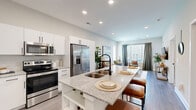 Located at 5700 Crossings Blvd in Nashville, Tennessee, this one-bedroom, one-bathroom residence offers a thoughtfully designed open-concept layout. The kitchen is a standout feature, equipped with stainless steel appliances including a French door refrigerator, electric range, and built-in microwave. Crisp white cabinetry with matte black hardware pairs elegantly with granite countertops, which extend onto a spacious island with an undermount double sink and bar seating — ideal for casual dining or entertaining. Light wood-look flooring runs throughout the main living areas, lending a clean, cohesive aesthetic. The living room is bright and welcoming, with large windows dressed in blinds and floor-length curtains that invite natural light while offering privacy. The bedroom is a calm retreat featuring a window with outdoor views, soft carpeting, and a notable ceiling height that adds a sense of openness. The bathroom offers a granite-topped vanity with white cabinetry, wood-look tile flooring, and direct access to a dedicated walk-in closet with built-in shelving. Recessed lighting throughout the home adds a polished finish, and neutral wall tones create a versatile, move-in-ready environment in this Nashville residence.