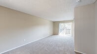 Located in Escondido, California, this single-floor unit offers a practical and well-organized layout comprising a combined kitchen and living area alongside a full bathroom. The living room is finished with neutral-toned carpet and warm beige walls, creating a calm and versatile space. A textured ceiling adds character, while multiple windows and a sliding glass door with vertical blinds allow natural light to fill the room and provide access to an outdoor area. A wall-mounted AC unit ensures year-round comfort. The kitchen features wood-look vinyl flooring, white cabinetry with ample storage, dark countertops, a stainless steel refrigerator, and a built-in dishwasher. A track lighting fixture provides targeted illumination over the workspace, and a sink with a window above it completes the functional setup. The bathroom continues the wood-look vinyl flooring found in the kitchen, maintaining a cohesive aesthetic. It includes a walk-in shower with white tile surround and a curved curtain rod, a toilet, and a vanity with dark countertop and brushed nickel hardware. The overall design is clean and neutral, offering a move-in-ready space in a well-connected Escondido location.