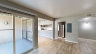 This single-floor residence offers a clean, modern aesthetic throughout its thoughtfully designed layout. The entry hallway welcomes you with light wood-look flooring, textured walls, and a ceiling-mounted HVAC vent, setting a neutral and functional tone from the start. The open-concept living and dining area is spacious and bright, featuring the same wood-look flooring, soft gray walls, and a textured ceiling. A sliding glass door leads directly to a private balcony, allowing natural light to pour into the space and offering pleasant outdoor views. The kitchen is a standout feature, showcasing dark gray cabinetry, a white subway tile backsplash, light stone countertops with a breakfast bar peninsula, and a full suite of stainless steel appliances including a refrigerator, range, microwave, and dishwasher. An additional room with wood-look flooring provides flexibility as a dining area or secondary living space. The bedrooms are carpeted for comfort, each featuring neutral gray walls, recessed window ledges, and blinds for privacy. The bathroom includes a tiled tub and shower surround, a vanity with a light countertop, and wood-look flooring. An electrical panel is conveniently located within the unit. Overall, the space presents a cohesive, move-in-ready environment with contemporary finishes throughout.