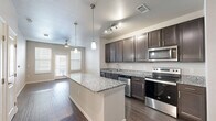 This efficiently designed 1-bedroom, 1-bathroom unit is laid out on a single floor, making smart use of its compact footprint. The open-concept kitchen and living area serves as the heart of the home, anchored by a central island topped with granite countertops that also doubles as additional prep and dining space. The kitchen is outfitted with rich dark-toned cabinetry, stainless steel appliances including a refrigerator, electric range, microwave, and dishwasher, and a undermount sink. Pendant lighting above the island and a track light fixture add a modern touch. Hardwood-style flooring runs throughout the main living area, lending warmth and continuity to the space. The living room benefits from natural light through multiple windows and a sliding glass door, with a ceiling fan adding both comfort and style. The bedroom offers a cozy, private retreat with a window for natural light and direct access to the closet and bathroom. The bathroom features a dark-toned vanity with a sink, a tub-shower combination, and recessed lighting. A dedicated closet provides practical storage. The unit's neutral color palette and consistent finishes create a cohesive, move-in ready environment throughout.