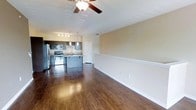 This single-floor residence offers an open-concept layout that maximizes flow and functionality throughout the living areas. Rich, dark hardwood flooring runs continuously across the space, adding warmth and a polished aesthetic to the interior. The living and dining areas are generously proportioned, with neutral warm-toned walls, white chair rail molding, and a ceiling fan that enhances comfort and air circulation.

The kitchen is a standout feature, seamlessly integrated into the open floor plan via a peninsula-style counter with bar seating. It is equipped with stainless steel appliances, including a refrigerator, electric range, and microwave, complemented by dark cabinetry and light-toned countertops. Pendant lighting above the peninsula and a dedicated track lighting fixture overhead provide both task and ambient illumination. A utility door adjacent to the kitchen offers additional access and convenience.

The overall ambiance is clean and contemporary, with a well-balanced combination of dark flooring, neutral walls, and modern fixtures. The open layout ensures excellent sightlines across the entire main living area, making the space feel airy and connected. This residence is thoughtfully designed to balance everyday practicality with a modern aesthetic.