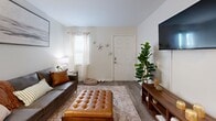 This 450 square foot apartment in Wilmington, NC, offers a well-designed living space with two bedrooms and one bathroom. The single-story layout maximizes efficiency, featuring a modern kitchen, comfortable living room, and a primary bedroom of 160 square feet.

The living area showcases a contemporary aesthetic with a leather sofa, decorative pillows, and a large abstract artwork. Natural light floods the space through windows adorned with sheer curtains. The kitchen boasts dark cabinetry contrasting with white appliances and light countertops, creating a sleek look. A small office nook adjacent to the kitchen provides a dedicated workspace.

Both bedrooms feature plush carpeting and ample natural light. The primary bedroom is adorned with blue accents, including a knitted throw and curtains, creating a serene atmosphere. Throughout the apartment, wood-look flooring adds warmth and continuity.

The thoughtful design incorporates storage solutions and decorative elements like potted plants and wall art, enhancing the overall ambiance. Despite its compact size, the apartment offers a harmonious blend of style, comfort, and functionality, making efficient use of every square foot.