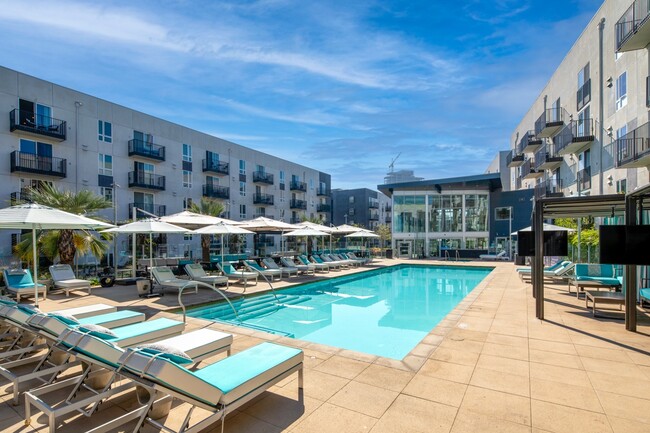 a swimming pool with lounge chairs and umbrellas at an apartment building - Aliso