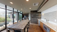 Located at 624 Yale Avenue North in Seattle's South Lake Union neighborhood, this single-floor amenity space is a refined blend of industrial warmth and modern design. Throughout the interior, wide-plank hardwood-style flooring and richly textured reclaimed wood wall panels establish a cohesive, nature-inspired aesthetic that feels both inviting and contemporary.

The lounge area serves as a central gathering point, anchored by a striking stacked-stone fireplace wall with a mounted flat-screen television and a built-in hearth. Comfortable seating arrangements — including leather and fabric chairs — create an atmosphere ideal for relaxation or socializing.

A dedicated dining area features a substantial rustic wood communal table surrounded by mixed seating, positioned adjacent to a functional kitchenette. The kitchenette is appointed with warm wood cabinetry, stone countertops, a sink, microwave, and a glossy subway tile backsplash, making it well-suited for hosting and entertaining.

Floor-to-ceiling black-framed glass doors and windows flood the space with natural light while providing direct access to an outdoor deck area, where landscaped greenery and city views can be enjoyed. A cozy nook framed in reclaimed wood offers an intimate retreat within the larger open layout. Decorative touches, including a stacked-slate accent column and curated wall art, complete the refined, Pacific Northwest-inspired character of this space.