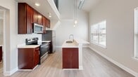 Located at 200 East 5th Avenue in York, PA, this two-story residence offers a thoughtfully designed layout across two floors. The main level provides a generous living and kitchen area bathed in natural light from multiple windows, with light-toned hardwood-style flooring running throughout. The kitchen is a standout feature, showcasing rich cherry wood cabinetry, a large center island with a crisp white countertop and pendant lighting, and a full suite of stainless steel appliances including a refrigerator, electric range, and microwave. Soaring ceilings lend an expansive, open feel to the main living space, with exposed ductwork adding an industrial touch. A hallway with access to a utility panel connects the key areas of the main level. The upper floor is home to the private bedroom, which features plush carpeting, impressively tall ceilings, a closet, and a calm, neutral palette. The full bathroom is clean and functional, equipped with a combined tub and shower, a cherry wood vanity with a white countertop, and light wood-tone flooring. Throughout the residence, neutral gray walls and white trim create a cohesive, modern aesthetic ideal for comfortable everyday living.