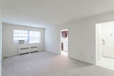 This single-floor unit offers a straightforward and functional layout designed for comfortable everyday living. The main living area is generously proportioned, featuring neutral wall-to-wall carpeting, clean white walls, and a large window that allows natural light to fill the room. A baseboard radiator and wall-mounted air conditioning unit provide year-round climate control. The entry foyer is finished with tile flooring and leads conveniently into the living space.

The kitchen is a standout feature, equipped with rich dark espresso-toned cabinetry that extends to the ceiling for ample storage. Granite-style countertops provide a clean, modern work surface, complemented by a white gas range and a full-sized refrigerator. Tile flooring completes the kitchen's practical finish.

The bedroom is a well-sized, carpeted retreat featuring a ceiling fan with light fixture and direct access to a closet, offering solid storage. Its neutral palette provides a calm and versatile backdrop.

The bathroom is bright and functional, featuring white subway tile wainscoting, a vanity with an integrated sink, a toilet, and a combination tub and shower. A large window brings in natural light while a wall mirror and overhead storage add everyday convenience. The space as a whole presents a clean, move-in ready environment.