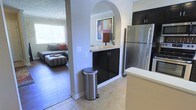 This two-floor residence offers a thoughtfully designed layout that balances functionality and modern style. The kitchen is a standout space, equipped with stainless steel appliances, including a full-size refrigerator, and sleek dark cabinetry that provides ample storage. Light countertops complement the cabinetry, while tile flooring grounds the space with a clean, polished look. A distinctive arched passageway connects the kitchen to the living area, adding an elegant architectural detail that enhances the open flow between spaces. The living area, visible through the arch, features warm hardwood-style flooring, soft neutral tones, and abundant natural light streaming through a large window. Comfortable seating and accent pillows in muted earth tones contribute to a welcoming, relaxed ambiance. The light gray walls throughout create a cohesive, airy atmosphere that ties the spaces together. Subtle design details, such as the decorative artwork and warm lamp accents, add personality without overwhelming the space. Spanning two floors, this residence offers generous room to live, with a versatile layout suited to a variety of lifestyles. The combination of modern finishes, architectural character, and natural light makes this a bright and inviting place to call home.