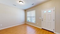 This two-story home is thoughtfully laid out across two floors, with the ground floor housing the main living and kitchen areas and the upper floor dedicated primarily to bedrooms. The ground floor features a combined kitchen and living room area finished with warm hardwood-style flooring that extends through the main spaces. The kitchen includes wood cabinetry, a full-size refrigerator, and a pendant-lit dining nook framed by a window overlooking the outdoors. The living area is bright and open, with a white panel front door, a window fitted with blinds, and a flush-mount ceiling light.

The upper floor contains four bedrooms, including a spacious primary bedroom equipped with a ceiling fan and light fixture. The remaining bedrooms feature neutral carpet, double-door closets, and windows that provide natural light and outdoor views. Three bathrooms are distributed across the home, one of which features tile flooring and a vanity with wood cabinetry and a white countertop. Hallways connect the rooms on both levels, with two staircases facilitating circulation. Throughout, neutral beige tones, white trim, and clean finishes contribute to a consistent, understated aesthetic.
