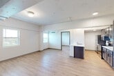 This 2-bedroom, 1-bathroom unit offers a thoughtfully designed layout across a single floor, blending modern finishes with industrial character. Light wood-style flooring runs throughout the entire space, creating a warm and cohesive aesthetic. The open living area is bright and airy, with multiple windows allowing natural light to fill the room, complemented by exposed structural ceiling elements and visible conduit that add a loft-inspired feel.

The kitchen is a standout feature, equipped with rich dark-stained cabinetry, white countertops, and a full suite of stainless steel appliances including a refrigerator, electric range, and built-in microwave. A peninsula with a sink provides additional prep space and casual dining potential, while recessed lighting keeps the area well-lit.

The primary bedroom offers a comfortable footprint with a ceiling fan, a window with outdoor greenery views, and a sliding glass door for added versatility. The second bedroom mirrors this layout with its own window and ceiling fan. The bathroom features dark wood cabinetry, white countertops, light tile-style flooring, and matte black hardware for a modern touch. The entryway includes a wall-mounted mini-split HVAC unit for individual climate control.