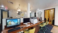 Located at 1006 South Main Street in Moscow, Idaho, this single-floor amenity space combines functional workspaces with inviting lounge areas in a thoughtfully designed interior. The computer lab anchors the space, featuring a long, polished wood countertop lined with desktop computers, a multifunction printer, and rolling chartreuse task chairs. Bold motivational wall text and eclectic pendant globe lights add energy and personality to the area. Dark wainscoting panels on one wall provide a striking contrast to the bright, open layout.

Adjacent to the computer lab, semi-private booth seating with yellow upholstered backs and wood-top tables offers comfortable spots for collaborative work or casual gatherings. Pendant lighting and textured accent walls give this zone a lively, curated feel. A separate lounge area near the exterior entrance features a pair of tufted emerald green armchairs set against natural light from windows and glass doors leading outside.

A private conference room provides a more formal setting, equipped with a herringbone-patterned wood table, leather chairs, and a wall-mounted flat-screen display — ideal for meetings or group study. Tucked behind dramatic floor-to-ceiling gold drape curtains, a cozy retreat area offers navy blue sofas arranged around a live-edge wood coffee table on warm hardwood flooring, creating an intimate and relaxed atmosphere.
