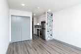 Located on the third floor in Seattle's Ballard neighborhood, this single-level studio presents a thoughtfully designed open-concept layout with modern finishes throughout. Wood-look plank flooring runs continuously across the living and kitchen areas, grounding the space in a warm, contemporary aesthetic.

The kitchen is outfitted with white flat-front cabinetry featuring brushed metal hardware, white quartz countertops, and a gray horizontal tile backsplash. Stainless steel appliances include a dishwasher, electric range, built-in microwave, and refrigerator. The galley-style configuration provides efficient workflow and ample storage.

The living area is defined by a distinctive geometric accent column finished in a white lattice pattern with blue and gray triangular insets, serving as a visual partition between the kitchen and main living space. A large closet with sliding gray doors provides substantial built-in storage.

A glass-paneled door opens to a private outdoor balcony, accompanied by floor-to-ceiling windows that invite generous natural light and offer views of the surrounding Ballard streetscape and greenery. The clean white walls and recessed lighting contribute to a bright, open ambiance throughout.