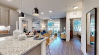 This thoughtfully designed one-bedroom, two-bathroom residence in Austin, TX offers a modern open-concept layout that seamlessly connects the kitchen and living areas. The kitchen is a standout feature, boasting granite countertops, a central island with pendant lighting, gray flat-front cabinetry, a white subway tile backsplash, open shelving, and a full suite of stainless steel appliances. Wood-look flooring flows throughout, lending warmth and continuity across the space.

The living room is bright and inviting, anchored by a ceiling fan and large sliding glass doors that flood the room with natural light and provide access to an outdoor area with open views of the surrounding greenery. Recessed lighting adds to the well-lit ambiance throughout the common areas.

The bedroom is a comfortable retreat, featuring large windows with tree-lined views, a ceiling fan, and ample closet space supported by two dedicated closets. The two bathrooms include a tub-shower combination finished with large-format neutral tile, offering a clean and contemporary aesthetic.

Overall, the residence presents a cohesive modern design with neutral tones, quality finishes, and a functional layout well-suited for everyday living in the Austin area.