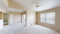 This single-story residence offers a well-organized layout with a warm, neutral color palette throughout. The main living area is a standout feature, boasting vaulted ceilings that enhance the sense of openness and volume. A ceiling fan with a brass fixture is centrally mounted, contributing both function and a classic aesthetic. Plush wall-to-wall carpeting extends across the living and bedroom areas, adding comfort underfoot. Natural light enters through a large window fitted with vertical blinds and a sliding glass door that opens to an outdoor patio or balcony, further brightening the space.

The kitchen features warm-toned wood cabinetry, laminate countertops, and durable wood-look vinyl flooring, providing a practical and functional cooking area. Adjacent rooms connect smoothly, maintaining a cohesive flow throughout the unit. The bedrooms are carpeted and generously sized, with one offering a walk-in closet equipped with built-in shelving and hanging rods. A bathroom includes a wide vanity with a large mirror, a Hollywood-style light bar, laminate countertop, and wood-look flooring, complemented by a combined tub and shower. The overall ambiance is clean, neutral, and move-in ready.