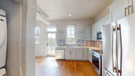 This single-floor unit in Columbia, SC, offers a thoughtfully designed interior with a clean, modern aesthetic. The kitchen serves as a standout feature, showcasing white shaker-style cabinetry with gold and silver hardware, light quartz countertops, and a distinctive striped tile backsplash. Stainless steel appliances, including a built-in microwave, dishwasher, and range, provide a polished, functional workspace. Open shelving flanks the sink window, allowing natural light to pour in while offering views of the outdoors. A door from the kitchen leads directly to an outdoor area, enhancing accessibility and ventilation.

Warm-toned hardwood flooring extends throughout the main living areas and bedrooms, lending continuity and a welcoming feel. The bedrooms are bright and simply designed, with white walls, natural light from slatted-blind windows, and generous closet space featuring dual bifold doors and built-in rods for ample storage.

The bathroom presents a contrasting design with large-format marble-look tile flooring, a white vanity with dark countertops and matte black hardware, and a walk-in shower enclosed by a striking black-framed glass door. The overall interior maintains a cohesive palette of whites and neutrals, creating a bright, modern, and move-in-ready living environment.