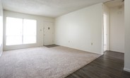 This single-floor residence presents a practical and well-organized layout across several distinct spaces. The galley-style kitchen is efficiently designed, featuring white cabinetry lining both walls, speckled laminate countertops, a stainless steel double sink, and black appliances including a refrigerator, range, and dishwasher. Wood-look vinyl plank flooring runs the length of the kitchen, and a textured ceiling adds a classic touch. A door at the end of the kitchen provides convenient secondary access.

The living area is a generously proportioned room with plush wall-to-wall carpeting and neutral white walls. A large sliding window allows natural light to fill the space. An adjacent transitional area connects the living room to the rest of the unit, featuring wood-look flooring, a visible HVAC vent, and access to additional rooms.

The bedrooms are carpeted and bright, each featuring windows that bring in natural light and views of the surrounding area. One bedroom includes a walk-in closet with built-in shelving, offering practical storage. All rooms feature textured ceilings throughout.

The bathroom is neatly appointed with a white vanity cabinet, speckled countertop, a framed mirror, globe vanity lighting, and a full tub-shower combination with white tile surround.
