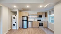 This thoughtfully designed 2-bedroom, 2-bathroom single-floor residence offers a well-organized layout with modern finishes throughout. Light wood-tone laminate flooring runs continuously through the living, kitchen, and bedroom areas, creating a cohesive and airy feel.

The kitchen is a standout feature, equipped with stainless steel appliances including a refrigerator, dishwasher, and range, complemented by light wood cabinetry, open shelving, and a classic white subway tile backsplash. A stacked washer and dryer unit is conveniently integrated into the kitchen area, adding everyday practicality.

The living area flows naturally from the kitchen and benefits from recessed lighting and a window that invites natural light. Both bedrooms are bright and well-proportioned, featuring large windows with outdoor views of the surrounding neighborhood and soft neutral wall tones. The primary bedroom offers a comfortable footprint, while the secondary bedroom includes a built-in closet with white bi-fold doors.

The bathrooms are elegantly appointed, featuring vertically laid white subway tile, striking dark marble-style floor tiles with gold veining, a wood-tone vanity, and a window for natural ventilation. The overall design aesthetic is clean, contemporary, and functional throughout.