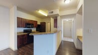 This single-floor, 2-bedroom, 2-bathroom residence offers a thoughtfully designed layout that balances open communal spaces with private retreats. Dark hardwood-style flooring runs throughout the main living areas, creating a warm and cohesive aesthetic, while light tile flooring transitions into the entry, kitchen, and bathrooms.

The spacious living area is highlighted by crown molding, a ceiling fan, and a large window that invites natural light and provides an airy feel. Track lighting and flush-mount ceiling fixtures provide ample illumination throughout. The open-concept design seamlessly connects the living room to the kitchen, which features rich dark-wood cabinetry, granite-style countertops, a full suite of black appliances including a refrigerator, electric range, microwave, and dishwasher, and a peninsula with bar-style seating.

A light-filled entry corridor leads to the main living spaces and includes a dedicated laundry area. Both bathrooms are finished with light ceramic tile flooring, and one features a full tub-shower combination with tile surround. The bedrooms are generously proportioned with continued hardwood-style flooring. Crown molding details and consistent neutral wall tones throughout lend the residence a polished, cohesive character.