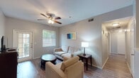 Located at 10127 State Highway 16 S in San Antonio, Texas, this single-floor unit offers a practical and comfortable layout designed with everyday functionality in mind. Wood-look flooring flows consistently throughout the space, complementing the neutral gray tones on the walls and creating a cohesive, modern aesthetic.

The living area is welcoming and generously sized, featuring a ceiling fan with integrated lighting and a large window alongside a glass-paned door that opens to a private patio, allowing ample natural light to fill the room. The space flows naturally into a dedicated dining area and a well-equipped kitchen. The kitchen is outfitted with two-tone cabinetry — white upper cabinets paired with dark lower cabinets — black appliances including a refrigerator, range, and dishwasher, and a light-toned stone countertop that extends to a convenient breakfast bar.

A hallway connects the living areas to two comfortably sized bedrooms, each equipped with a ceiling fan, natural light from windows with blinds, and wood-look flooring. The bathroom features a wide vanity with a stone countertop, dark cabinetry, a large mirror, and a shower-tub combination. The layout is completed by a dedicated dining space and additional storage throughout, making this unit a functional and inviting residence.