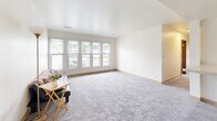 Located at 1209 N Dakota Ave in Ames, Iowa, this single-floor, 4-bedroom, 2-bathroom unit offers a practical and functional layout well-suited for shared living. The combined living and dining area flows seamlessly from the carpeted living room—filled with natural light from a large bank of front-facing windows—into the tiled dining space, which features a ceiling fan overhead. The kitchen is efficiently designed with dark-stained cabinetry, granite-look countertops, tile flooring, and full appliances including a refrigerator, electric range, and built-in microwave. The four bedrooms are carpeted and feature neutral walls, wood-trimmed doors, and ample room for furnishings. The primary bathroom includes a shower/tub combo with a decorative curtain, a modern floating vanity with a clean white basin, and a wood-framed medicine cabinet. The second bathroom is more compact, featuring a wall-mounted sink, tile flooring, and a mirrored medicine cabinet. A dedicated laundry room with side-by-side washer and dryer units and overhead cabinetry adds everyday convenience. The unit's clean, neutral palette and functional design make it a solid residential option in Ames.