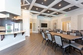 Located at 4225 Johns Creek Pkwy in Suwanee, Georgia, this single-floor community space is thoughtfully designed to accommodate a variety of functions and social interactions. The layout encompasses several distinct zones, each finished with consistent, upscale detailing throughout.

The main gathering hall is a standout feature, boasting coffered ceilings with dark-painted recesses that add architectural depth and elegance. Multiple long dining tables with upholstered chairs fill the room, making it well-suited for group meals or events. Large windows dressed in white drape panels and horizontal blinds flood the space with natural light and offer views of the surrounding greenery.

A dedicated conference or meeting room adjoins the main hall, featuring intricate wainscoting and decorative wall paneling in a geometric pattern. A sizable rectangular table surrounded by padded chairs provides a refined setting for formal gatherings or smaller meetings.

The lounge area offers a more relaxed atmosphere, furnished with a neutral-toned sofa, accent chairs, and side tables. Oversized windows continue the theme of abundant natural light throughout.

The kitchen is fully equipped with rich dark cabinetry, granite countertops, a large center island with a cooktop, stainless steel appliances including double wall ovens, and a prominent overhead ventilation hood — ideal for catering or community cooking events.