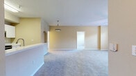 This single-floor residence offers a thoughtfully designed layout with a warm, neutral color palette of soft beige tones and bright white trim throughout. The spacious open-concept living and dining area is finished with plush carpeting and features a decorative pendant light, a ceiling fan, and an arched architectural detail that adds character to the space. A dedicated entryway provides a welcoming transition into the main living area.

The kitchen is well-equipped with stainless steel appliances, including a refrigerator, electric range, and over-the-range microwave. Crisp white cabinetry offers generous storage, complemented by light-toned countertops and durable wood-look flooring that extends throughout the kitchen and bathroom areas.

The bedrooms are carpeted and generously sized, each benefiting from ceiling fans and windows that invite natural light and offer views of surrounding greenery. The primary bedroom includes direct access to a private bathroom, enhancing convenience and privacy.

The bathroom is finished with a wide vanity featuring a white countertop, undermount sink, and a large mirror with overhead lighting. A dedicated in-unit laundry room accommodates a full-size washer and dryer with overhead wire shelving for added storage. Overall, the space presents a clean, functional, and comfortable living environment.