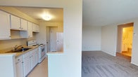 This single-floor residence offers a thoughtfully laid-out living space with a clean, neutral aesthetic throughout. The open-concept kitchen is equipped with white cabinetry, a electric range, a refrigerator, and a sink, seamlessly connecting to the adjacent living and dining areas via a half-wall peninsula. The kitchen features light vinyl flooring, while the living and bedroom areas are finished with wall-to-wall carpet in a warm neutral tone. A textured ceiling adds character throughout the main living spaces.

The living room is bright and spacious, featuring large sliding glass doors dressed with vertical blinds that open to a private balcony. From the balcony, stunning views of lush mature trees and a body of water beyond create a serene outdoor backdrop. A wall-mounted air conditioning unit and baseboard heating ensure year-round comfort.

The bedroom is generously sized with a window that invites natural light and offers additional outdoor views. A short hallway connects the bedroom to a full bathroom, which includes a tub-shower combination with white tile accented by colorful mosaic tile details, a vanity with sink, and mosaic tile flooring. An additional closet in the hallway provides convenient storage. The overall ambiance is calm, bright, and functional.