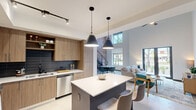 Located at 4181 Davie Dr in Davie, FL, this contemporary two-story home offers a thoughtfully designed layout across two floors. The main level impresses with soaring double-height ceilings that amplify the sense of space throughout the open-concept living and dining areas. Large windows and glass doors flood the living room with natural light and provide views of the outdoors, while a sleek floating staircase set against a striking exposed brick accent wall adds an industrial-chic character to the space. The kitchen is a standout feature, equipped with warm wood cabinetry, a dark tile backsplash, stainless steel appliances, and a navy blue center island with a crisp white countertop and bar seating — perfect for casual dining. A dedicated office on the main level provides a quiet workspace. The upper level hosts the generously sized primary bedroom, complete with hardwood flooring, a walk-in closet, and an en-suite bathroom featuring a dual-sink vanity with dark wood cabinetry and a large mirror. Additional bathrooms include a clean, neutral-toned bath with a soaking tub. With three full bathrooms, two bedrooms, and a versatile office, this home delivers a well-rounded and functional living experience with modern finishes throughout.