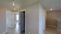 This three-floor property is designed with functionality and simplicity in mind, featuring a neutral color palette of soft beige and white tones that lend a clean, understated aesthetic throughout. The hallway area visible in the image showcases light-toned tile flooring, which transitions seamlessly between spaces, contributing to a cohesive look. White trim and door frames provide crisp contrast against the warm beige walls, adding a polished finish to the interior.

A built-in shelved closet is positioned along the hallway, offering practical storage directly accessible from the corridor. The shelving unit is enclosed with a standard door, keeping the space tidy and organized. Multiple doorways branch off from this central hallway, suggesting a well-connected floor plan that allows easy navigation between rooms. Natural light filters in from a window visible in the background, brightening the passage and contributing to an open, airy feel.

Recessed ceiling lighting provides consistent illumination throughout the hallway. The angled ceiling detail near the closet area hints at architectural variation across the levels. Overall, the space presents a straightforward, well-maintained interior suited for comfortable everyday living.
