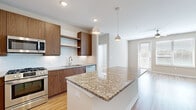 This single-floor residence showcases a thoughtfully designed open-concept layout with consistent light hardwood flooring connecting all living areas. The kitchen serves as a central highlight, featuring rich wood-tone cabinetry, granite countertops, and a full suite of stainless steel appliances including a gas range, built-in microwave, dishwasher, and French door refrigerator. A subway tile backsplash adds a clean, modern touch, while a large island with a granite surface provides additional workspace and casual seating. Pendant lighting illuminates the kitchen and flows into the open living area, which benefits from natural light through large windows and a glass-panel exterior door. A ceiling fan overhead enhances comfort in the living space. The bedrooms are generously proportioned, each featuring ceiling fans, neutral walls, and ample natural light. The primary bathroom includes a glass-enclosed shower with tile surround, a wood-tone vanity with granite countertop, and direct access to a spacious walk-in closet outfitted with wire shelving systems for organized storage. The overall aesthetic is clean, contemporary, and move-in ready.