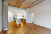 Located at 2681 Tagore Ave NE in Redmond, WA, this 2-bedroom, 2-bathroom residence offers a compelling blend of industrial and modern design across a single floor. The open-concept living and kitchen area is defined by striking exposed concrete ceilings and warm hardwood flooring, creating a loft-inspired ambiance. Exposed concrete columns add architectural character throughout the main living space, which receives generous natural light through large sliding glass doors that lead to a private patio overlooking lush greenery.

The kitchen is well-appointed with stainless steel appliances, including a French door refrigerator, electric range, and microwave. Two-tone cabinetry — white uppers paired with natural wood lowers — surrounds the space, complemented by a central island with a clean white countertop and pendant lighting overhead.

Both bedrooms are carpeted and bright, with windows framing outdoor views. The primary bedroom is generously sized and benefits from ample closet storage. In total, five closets are distributed throughout the unit, ensuring exceptional storage capacity. The bathrooms feature hardwood-style flooring, wood-toned vanities, and clean, functional fixtures. A well-organized hallway with built-in wire shelving adds further practical storage to this thoughtfully designed Redmond residence.