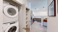 This well-appointed single-floor residence offers two bedrooms, two bathrooms, and a thoughtfully designed layout that maximizes functionality and comfort. Light wood-tone flooring runs throughout, creating a cohesive and airy aesthetic across the entire space.

The kitchen is a standout feature, showcasing a contemporary design with two-tone cabinetry — upper white cabinets paired with warm wood-finish lower cabinets — complemented by a white tile backsplash and stainless steel appliances including a French door refrigerator, range, microwave, and dishwasher. A central island with seating provides additional prep space and casual dining. Sleek pendant lighting overhead adds a modern finishing touch. Adjacent to the kitchen, a dedicated closet houses a stacked washer and dryer unit alongside built-in shelving.

The living room is bright and open, benefiting from a large sliding glass door that frames outdoor views and fills the space with natural light. The primary bedroom is a comfortable retreat with clean white walls and direct closet access. The second bedroom features dual windows, offering ample natural light. The primary bathroom includes a glass-enclosed tiled shower, while the second bathroom offers a full tub-shower combination, both finished with consistent white tile and wood-look flooring.