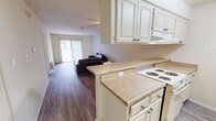 This single-story, 820-square-foot apartment offers a well-organized layout with 2 bedrooms, 2 bathrooms, a combined kitchen and living area, and a closet. The kitchen features cream-toned cabinetry with a built-in range, overhead ventilation hood, full-size refrigerator, and a peninsula breakfast bar that separates it from the dining and living areas. Light wood-style flooring runs throughout the unit, contributing to a clean, cohesive aesthetic. The living room is bright and open, highlighted by a large sliding glass door with vertical blinds that provides direct access to an outdoor patio and fills the space with natural light. The primary bedroom measures 150 square feet and includes a ceiling fan, a window with exterior views, and direct access to one of the two bathrooms, which features a single vanity with a wide mirror and medicine cabinet. The second bedroom is a more compact space with its own window and closet access. The second bathroom includes a full tub/shower combination, a single vanity with cabinetry, and wood-style flooring. Neutral wall tones and consistent flooring throughout the unit create a cohesive, move-in-ready environment suited for individuals or small households.
