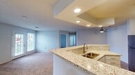 This single-floor home accommodates four bedrooms and two full bathrooms within a thoughtfully arranged layout. The open-concept kitchen serves as a central feature, showcasing granite-look countertops, a peninsula with a double-basin sink, white shaker cabinetry, and stainless steel appliances including a refrigerator, range, and microwave. Recessed lighting highlights a stepped ceiling detail above the kitchen and living area, lending architectural interest to the space. A ceiling fan adds both function and style to the adjoining living area, which features neutral carpet flooring and natural light from windows with blinds.

The bedrooms are carpeted and simply designed, with the primary bedroom offering a walk-in closet fitted with wire shelving. Each room benefits from natural light via standard windows. Both bathrooms are equipped with tub-shower combinations, granite-look vanity countertops, and warm hardwood-style flooring. The dedicated laundry room includes overhead white cabinetry for storage and accommodates a full-size washer and dryer. Throughout the home, a consistent light gray color palette and clean finishes contribute to a bright, cohesive aesthetic.