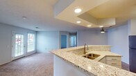 This single-floor home accommodates four bedrooms and two full bathrooms within a thoughtfully arranged layout. The open-concept kitchen serves as a central feature, showcasing granite-look countertops, a peninsula with a double-basin sink, white shaker cabinetry, and stainless steel appliances including a refrigerator, range, and microwave. Recessed lighting highlights a stepped ceiling detail above the kitchen and living area, lending architectural interest to the space. A ceiling fan adds both function and style to the adjoining living area, which features neutral carpet flooring and natural light from windows with blinds.

The bedrooms are carpeted and simply designed, with the primary bedroom offering a walk-in closet fitted with wire shelving. Each room benefits from natural light via standard windows. Both bathrooms are equipped with tub-shower combinations, granite-look vanity countertops, and warm hardwood-style flooring. The dedicated laundry room includes overhead white cabinetry for storage and accommodates a full-size washer and dryer. Throughout the home, a consistent light gray color palette and clean finishes contribute to a bright, cohesive aesthetic.