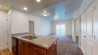 This single-floor residence offers a thoughtfully designed layout that balances open communal spaces with private retreats. The kitchen serves as a central highlight, featuring rich warm-toned wood cabinetry, granite countertops, a double-basin sink, and a full suite of black appliances including a range, microwave, refrigerator, and dishwasher. Durable hardwood-style flooring runs throughout the kitchen, while recessed lighting adds a polished finish overhead. A peninsula with a granite countertop and cabinetry below connects the kitchen to the open living and dining area, which is finished with plush wall-to-wall carpeting and ceiling-mounted light fixtures. Sliding glass doors with vertical blinds open to an outdoor space, filling the living area with natural light. The bedrooms are generously sized and carpeted, with one featuring a tray ceiling detail and a window overlooking greenery, and another equipped with a spacious reach-in closet with wire shelving behind arched double doors. A well-appointed hallway connects the private areas of the home. The bathroom includes a soaking tub and shower combo with tiled surround, a granite-topped vanity with warm wood cabinetry, a large mirror, and tile flooring. Throughout the residence, arched interior doors and consistent finishes contribute to a cohesive and comfortable aesthetic.