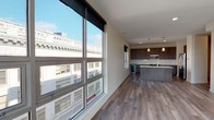 This single-floor unit at The Edge on 4th offers a well-designed open layout connecting the living area and kitchen. Large floor-to-ceiling windows flood the living space with natural light and frame dynamic urban views of the surrounding cityscape, complemented by wood-look plank flooring throughout the main areas.

The kitchen is a standout feature, outfitted with floor-to-ceiling wood-grain cabinetry in a warm taupe finish, light quartz countertops, a clean white tile backsplash, and a full suite of stainless steel appliances including a range, microwave, refrigerator, and a beverage cooler. Pendant lighting over the kitchen island adds a refined touch.

The bedrooms are carpeted for comfort, each receiving natural light through windows with roller shades and urban views. One bedroom includes a ceiling fan and a spacious walk-in closet with built-in shelving and hanging rods. Two bathrooms serve the unit — one featuring a glass-enclosed walk-in shower with light tile flooring, and the other offering a full tub-shower combo with wood-look vinyl flooring and a dark-toned vanity. The overall aesthetic is clean, contemporary, and well-suited for urban living.