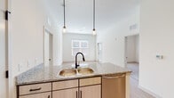 This well-appointed single-floor residence offers a clean, contemporary design with a cohesive neutral palette and quality finishes throughout. The open-concept kitchen serves as the heart of the home, featuring light wood cabinetry with matte black hardware, granite countertops, and a full suite of stainless steel appliances including a refrigerator, range, microwave, and dishwasher. A central island with a double-basin sink and pendant lighting overhead adds both functionality and style, while light wood-style flooring ties the space together seamlessly.

The living and dining areas extend naturally from the kitchen, benefiting from elevated ceilings and multiple windows dressed with blinds that invite generous natural light. The bedrooms offer a comfortable retreat, with plush carpeting in one room and light wood-style flooring in another, each accompanied by bright windows with exterior views.

The bathrooms are finished with the same granite countertops found in the kitchen, complemented by undermount sinks, light wood vanities with matte black hardware, and large mirrors. One bathroom includes a tub-shower combination. Throughout the residence, white panel doors, recessed lighting, and a consistent trim palette contribute to a polished, move-in-ready aesthetic that is both functional and inviting.