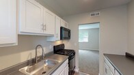 Located at 3232 January Ave in St. Louis, Missouri, this single-floor unit offers a clean, updated interior designed for comfortable everyday living. The kitchen is a functional highlight, featuring crisp white shaker-style cabinetry with brushed nickel hardware, sleek countertops, a stainless steel sink, and a full suite of black appliances including a gas range, over-the-range microwave, and dishwasher. Wood-style flooring grounds the kitchen, which opens through a defined archway into the adjacent living area. The living area is generously sized, finished with neutral wall-to-wall carpeting and a ceiling fan with light fixture. Natural light enters through large windows dressed with vertical blinds, creating a bright and airy atmosphere. An electrical panel is conveniently recessed into the living room wall. The bedroom is well-proportioned with soft carpet underfoot, two windows allowing ample natural light, and a ceiling fan. The bathroom features a full soaking tub and shower combination surrounded by large-format neutral tile, complemented by a small window that brings in natural light. Throughout the unit, neutral tones, clean lines, and thoughtful finishes create a cohesive and move-in ready environment.