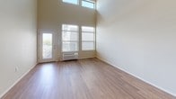 This well-appointed single-floor residence combines modern design with practical functionality throughout its thoughtfully arranged layout. The living area immediately impresses with dramatically high ceilings and an abundance of natural light streaming through large windows and a glass-paneled exterior door, creating an airy, open ambiance. Warm hardwood-style flooring extends throughout the main living and kitchen areas, lending a cohesive and inviting feel.

The galley-style kitchen is efficiently designed, featuring rich dark-wood cabinetry lining both sides, white countertops, a stainless steel refrigerator, stainless steel microwave, and an electric range. A peninsula with a single-basin sink and a pass-through window connects the kitchen to the living space, enhancing the open-concept flow.

The bedrooms offer plush wall-to-wall carpeting and windows providing outdoor views and natural light. Two full bathrooms serve the unit — one equipped with a soaking tub and shower combination, the other with a walk-in glass-enclosed shower — both featuring dark-wood vanities with white countertops and hardwood-style flooring.

A dedicated in-unit laundry area houses a full-size top-loading washer and dryer with overhead shelving for added storage convenience. The space presents a clean, neutral palette throughout, making it a versatile and functional home.