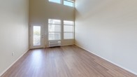 This well-appointed single-floor residence combines modern design with practical functionality throughout its thoughtfully arranged layout. The living area immediately impresses with dramatically high ceilings and an abundance of natural light streaming through large windows and a glass-paneled exterior door, creating an airy, open ambiance. Warm hardwood-style flooring extends throughout the main living and kitchen areas, lending a cohesive and inviting feel.

The galley-style kitchen is efficiently designed, featuring rich dark-wood cabinetry lining both sides, white countertops, a stainless steel refrigerator, stainless steel microwave, and an electric range. A peninsula with a single-basin sink and a pass-through window connects the kitchen to the living space, enhancing the open-concept flow.

The bedrooms offer plush wall-to-wall carpeting and windows providing outdoor views and natural light. Two full bathrooms serve the unit — one equipped with a soaking tub and shower combination, the other with a walk-in glass-enclosed shower — both featuring dark-wood vanities with white countertops and hardwood-style flooring.

A dedicated in-unit laundry area houses a full-size top-loading washer and dryer with overhead shelving for added storage convenience. The space presents a clean, neutral palette throughout, making it a versatile and functional home.
