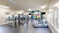 Located at 741 Plummer Rd in Huntsville, Alabama, this fitness center offers a generously sized, single-floor workout facility designed to accommodate a comprehensive range of exercise routines. The space is thoughtfully laid out to maximize functionality, with distinct zones dedicated to cardio training, strength equipment, and free weights.

The cardio section features Matrix-brand treadmills and elliptical machines positioned along a wall of multiple windows, allowing ample natural light to fill the space and offering views of the surrounding greenery and pool area. The strength training zone is equipped with a multi-station cable and weight machine setup, a full dumbbell rack, and various resistance machines, providing users with a thorough full-body workout experience. A colorful collection of medicine balls and stability balls adds versatility for functional fitness training.

Architectural highlights include a vaulted ceiling area with large arched windows accented by a bold green feature wall, lending visual interest and an open, airy feel to the room. Full-length mirrors line one wall, enhancing the sense of space and allowing users to monitor their form. Flat-screen TVs are mounted throughout for entertainment. Durable rubberized flooring covers the entire workout area, and flush fluorescent lighting ensures the space is consistently well-lit. The overall ambiance is clean, energetic, and well-maintained.