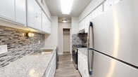 This 2-bedroom, 1-bathroom unit in Denver, Colorado offers a practical and comfortable single-floor layout. The galley-style kitchen is a standout feature, showcasing white shaker cabinets, granite-look countertops, a mosaic tile backsplash, and stainless steel appliances including a refrigerator and range. Wood-look plank flooring runs through the kitchen and living areas, while a ceiling fan with lighting anchors the open living space adjacent to the kitchen. A dedicated in-unit washer is conveniently tucked within the kitchen area alongside additional white cabinetry. Both bedrooms are carpeted and well-proportioned, with the primary bedroom offering a generous footprint and its own closet. The second bedroom features a window that invites natural light. The full bathroom includes a tub-shower combination and direct access to a walk-in closet, adding practical storage. Throughout the unit, textured ceilings and neutral wall tones create a clean, move-in-ready aesthetic. Multiple closets distributed across the floor plan provide ample storage. Hallways connect the living spaces efficiently, contributing to a cohesive and functional layout suited for everyday living in the Denver metro area.