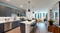 Located in Dallas, TX, this single-story residence at 2439 Beatrice St offers a well-appointed, open-concept layout with modern finishes and thoughtful design details throughout. The kitchen serves as a central highlight, featuring slate-gray shaker cabinetry, a white quartz countertop island with bar seating, stainless steel appliances, subway tile backsplash, and bold pendant lighting — all flowing seamlessly into the living area. The living space is warm and inviting, with wood-look flooring, large windows dressed in teal curtains that invite natural light, and a ceiling fan overhead. The primary bedroom is generously sized, benefiting from large windows with views of the outdoors and a walk-in closet with built-in shelving and dual hanging rods. The en-suite primary bathroom offers a double vanity with gray cabinetry, white quartz surfaces, matte black fixtures, and a glass-enclosed walk-in shower with white subway tile. A secondary bathroom mirrors the refined aesthetic with a long double vanity and a tub-shower combination. An additional bedroom provides a comfortable retreat with wall-mounted shelving and wood flooring. Throughout the home, consistent use of wood-look flooring, white walls, and matte black accents creates a cohesive, contemporary ambiance.
