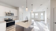 This thoughtfully designed single-floor residence offers a clean, modern aesthetic with high-quality finishes throughout. The open-concept layout seamlessly connects the kitchen and living room, creating an inviting and functional living space bathed in natural light from large windows.

The kitchen is a standout feature, showcasing crisp white shaker-style cabinetry with matte black hardware, a herringbone tile backsplash, and quartz countertops. A central island with a stainless steel undermount sink and an industrial-style spring faucet serves as both a prep space and casual dining area, accented by elegant pendant lighting. Stainless steel appliances, including a French door refrigerator, complete the space.

The living room is bright and airy, with light hardwood flooring, neutral white walls, and a glazed exterior door that fills the space with sunlight. The bedroom offers a comfortable retreat, featuring plush carpet flooring, a ceiling fan, natural light from windows with outdoor views, and closet access leading to the hallway.

The bathroom is finished in a minimalist style, with a sliding glass-enclosed shower, white vanity with quartz countertops, and matte black fixtures and hardware that echo the home's consistent design language. Light wood-tone flooring ties the space together cohesively.